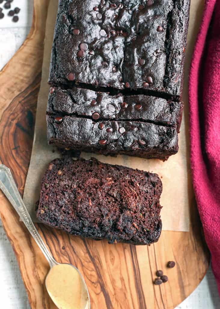 a loaf of paleo vegan chocolate zucchini bread with a slice laying on a cutting board