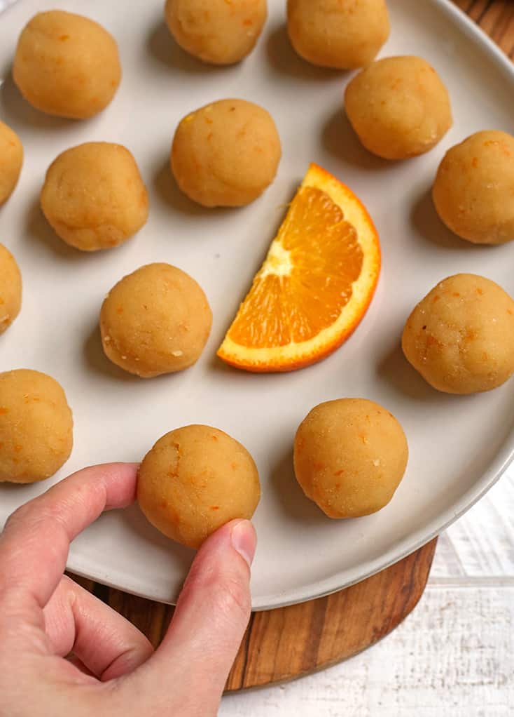 a plate of vegan orange creamsicle bites with a hand reaching for one