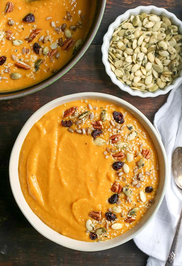 A bowl of butternut squash soup on a wooden table with a spoon to the right. 