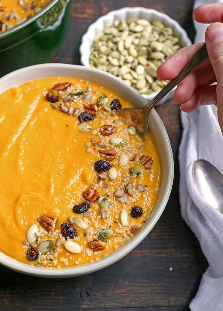 A bowl of butternut squash soup with nuts and seeds on top. 