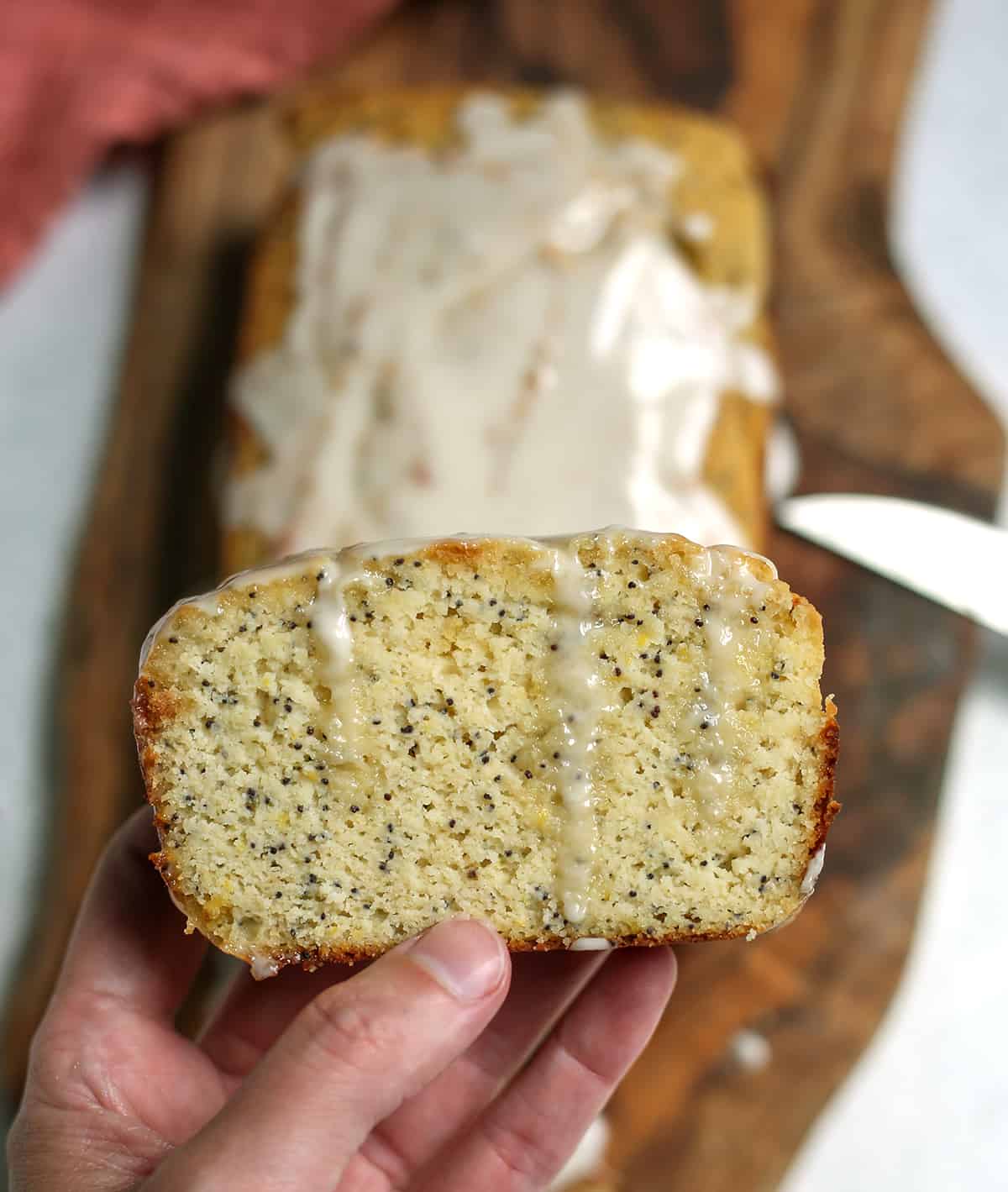 A hand holding a slice of lemon poppy seed bread with glaze dripping down. 