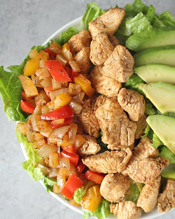 A close up of chicken, peppers and avocado over a bed of romaine. 