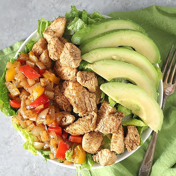 A Paleo Chicken Fajita Bowl with peppers and avocado on top and a fork next to it. 