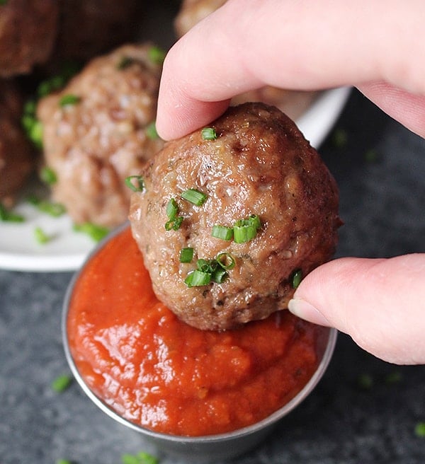 A paleo meatball being dipped into barbecue sauce. 