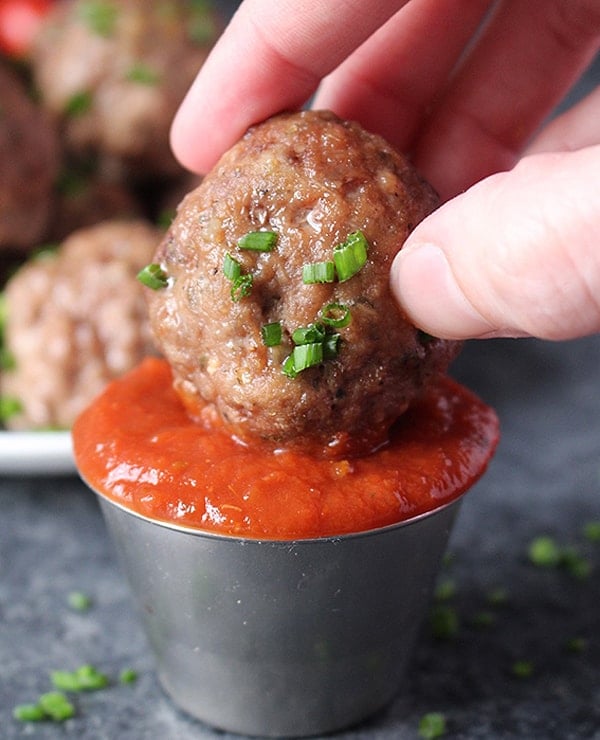 A meatball being dipped into barbecue sauce. 