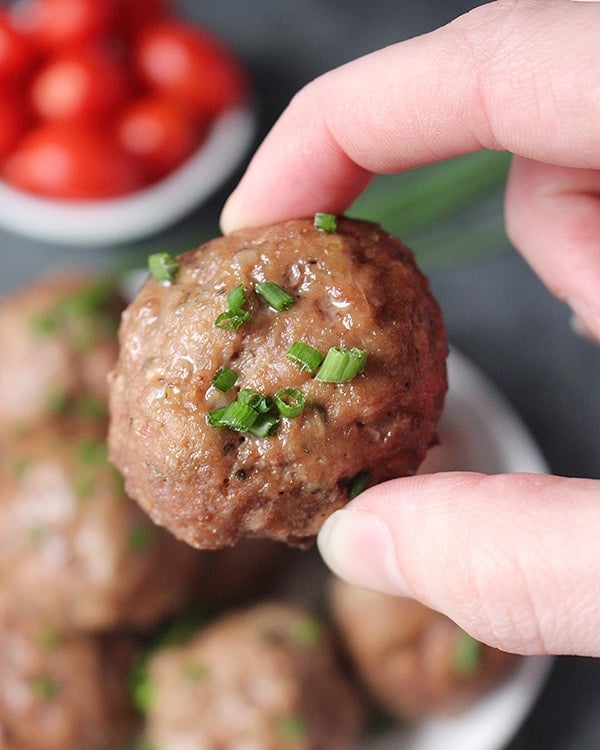 A hand holding a baked meatball. 