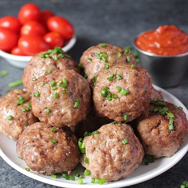 Oven baked meatballs  stacked on a plate with chives on top. 