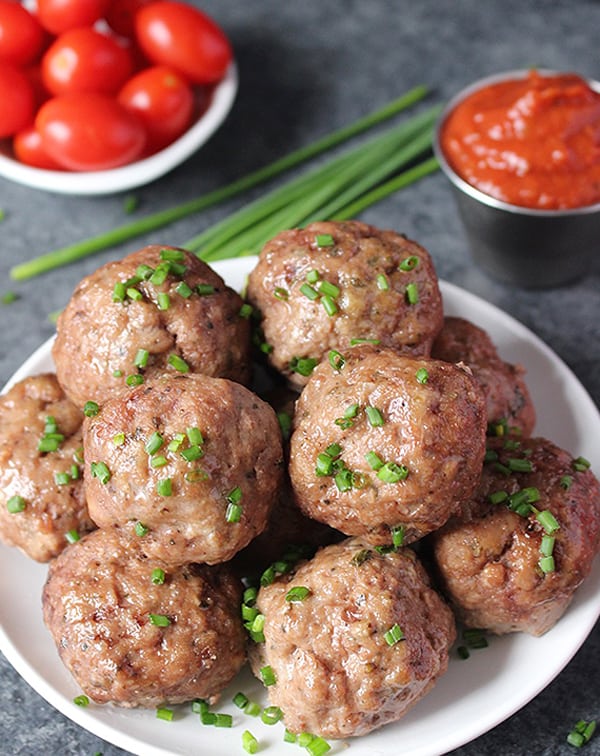 Oven baked meatballs on a plate with chives on top. 