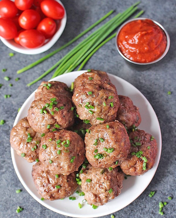 A plate of baked meatballs with chives on top. 