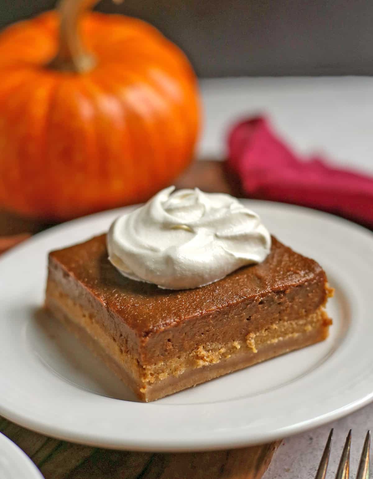 A piece of pumpkin pie on a small plate with a pumpkin in the background. 