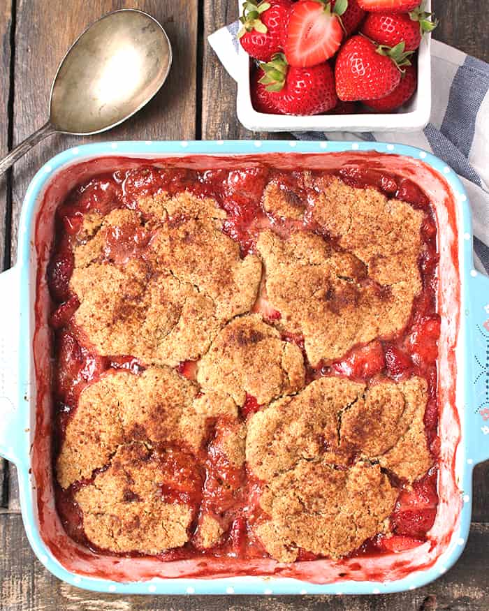 Paleo Strawberry Cobbler in a pan with some fresh strawberries above it. 