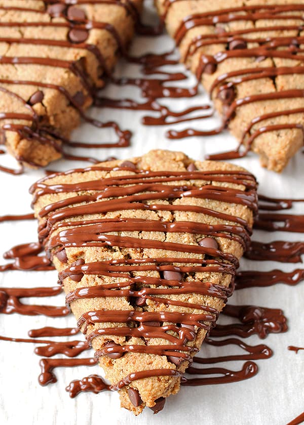 A chocolate chip scone with chocolate drizzle on a plate with a couple more behind it. 