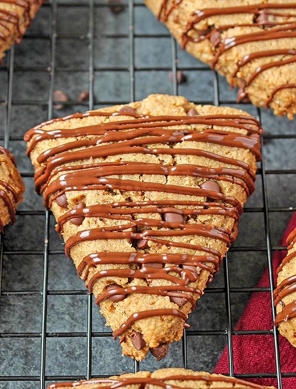 A chocolate chip scones with chocolate drizzle on a cooling rack.