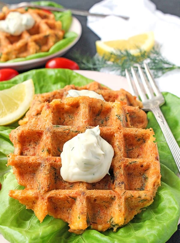 close view of salmon cake waffles on a lettuce bed with a dill sauce on top. 