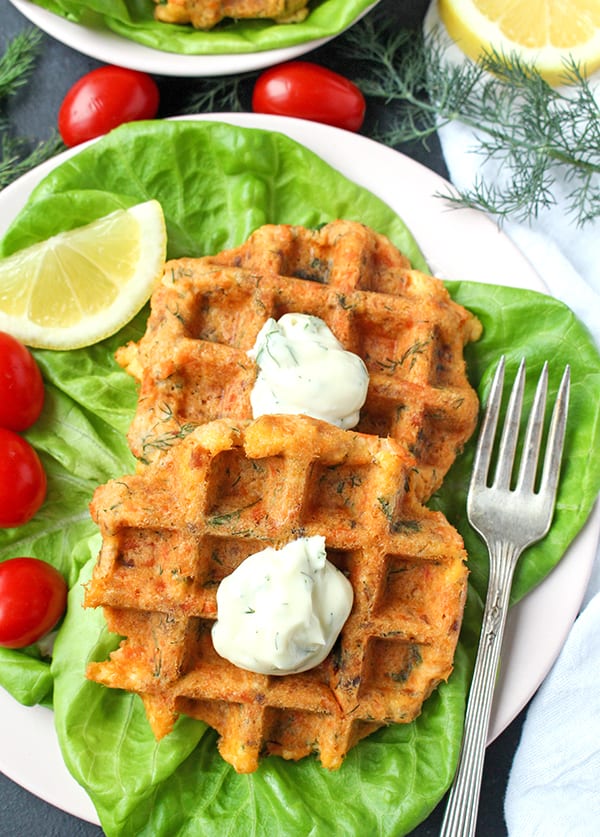 close view of salmon cake waffles on a lettuce bed with a dill sauce on top and a fork on the right. 