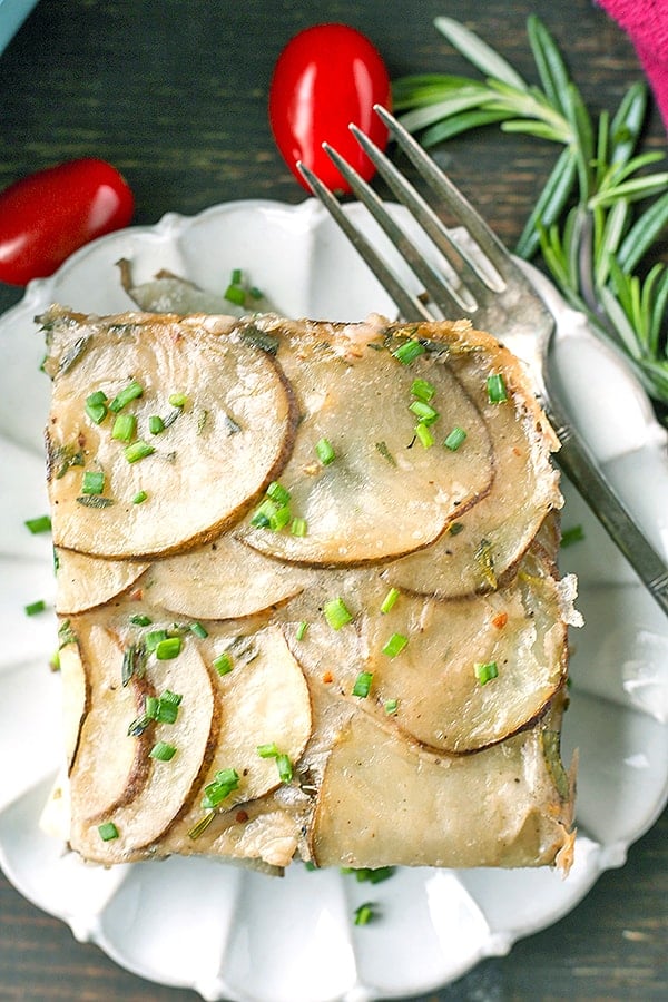 Scalloped potatoes on a plate with chives on top. 