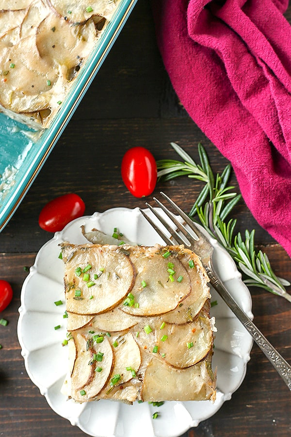 A serving of scalloped potatoes on a plate with rosemary on the side. 