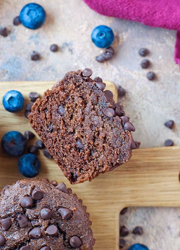 A gluten free chocolate muffin cut so the inside is showing, on a cutting board with chocolate chips around it. 