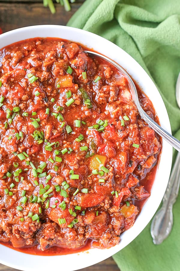 A full bowl of bean-less chili with a spoon in it. 
