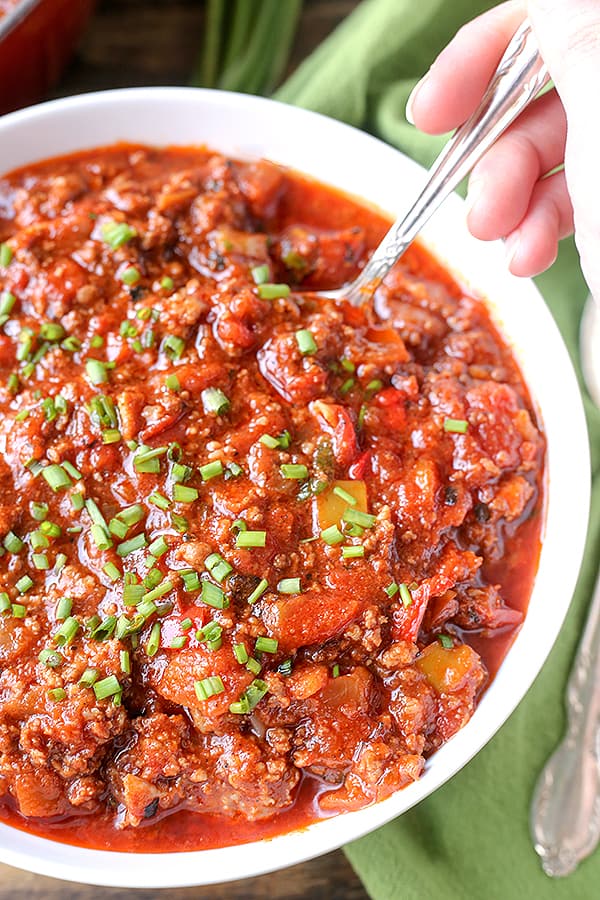 Bowl of chili with a spoon in it. Green onions on top of the chili. 