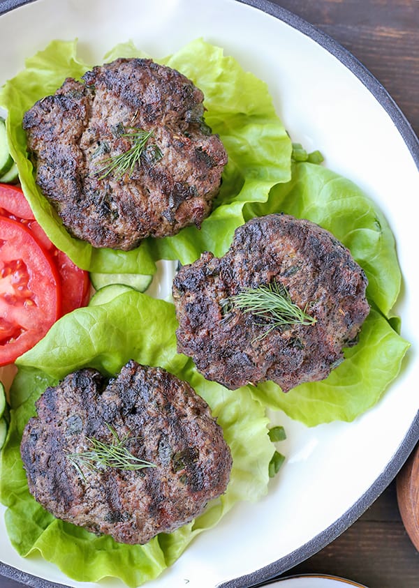 Gyro burgers on lettuce wraps on a plate with tomatoes. 