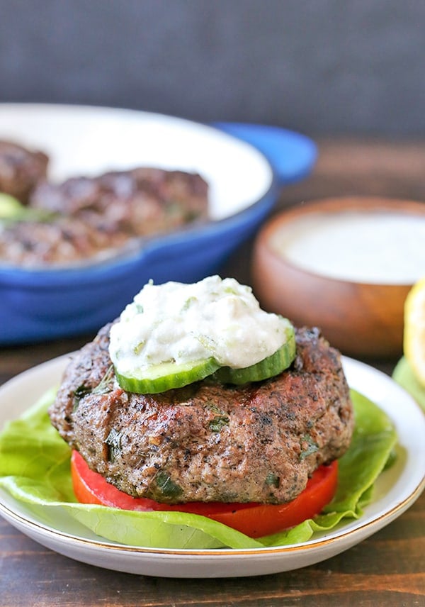 A gyro burger on a lettuce bun with tomato, cucumber and sauce. 