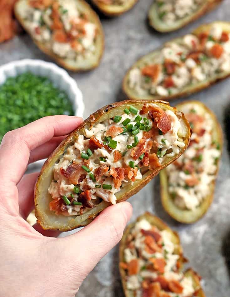 A hand holding a potato skin filled with chicken and bacon. 