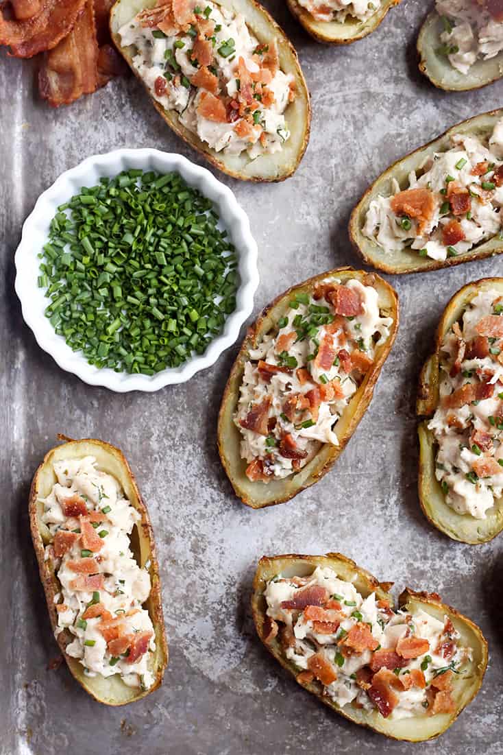potato skins on a sheet tray with chives in a bowl next to them. 