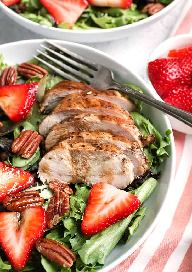 Close up of balsamic chicken on a bed of greens with strawberries 
