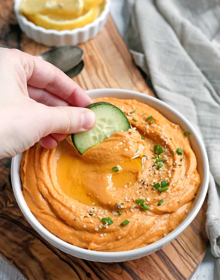 paleo hummus in a bowl with a cucumber being dipped