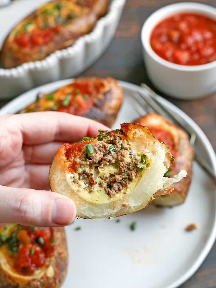 a hand holding a potato stuffed with taco meat and egg