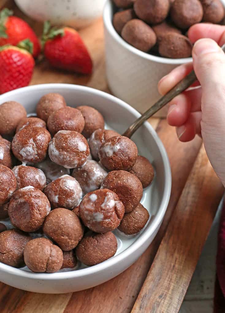 paleo nut free cocoa puffs with almond milk. A hand taking a bite. 