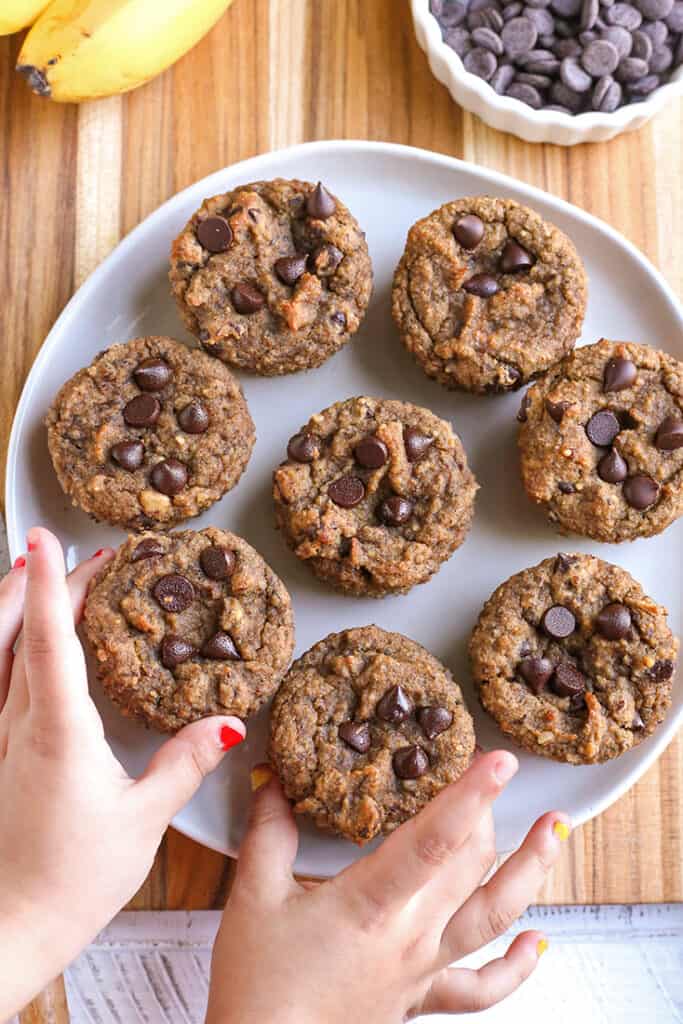 vegan paleo banana muffins on a plate with two small hands touching them