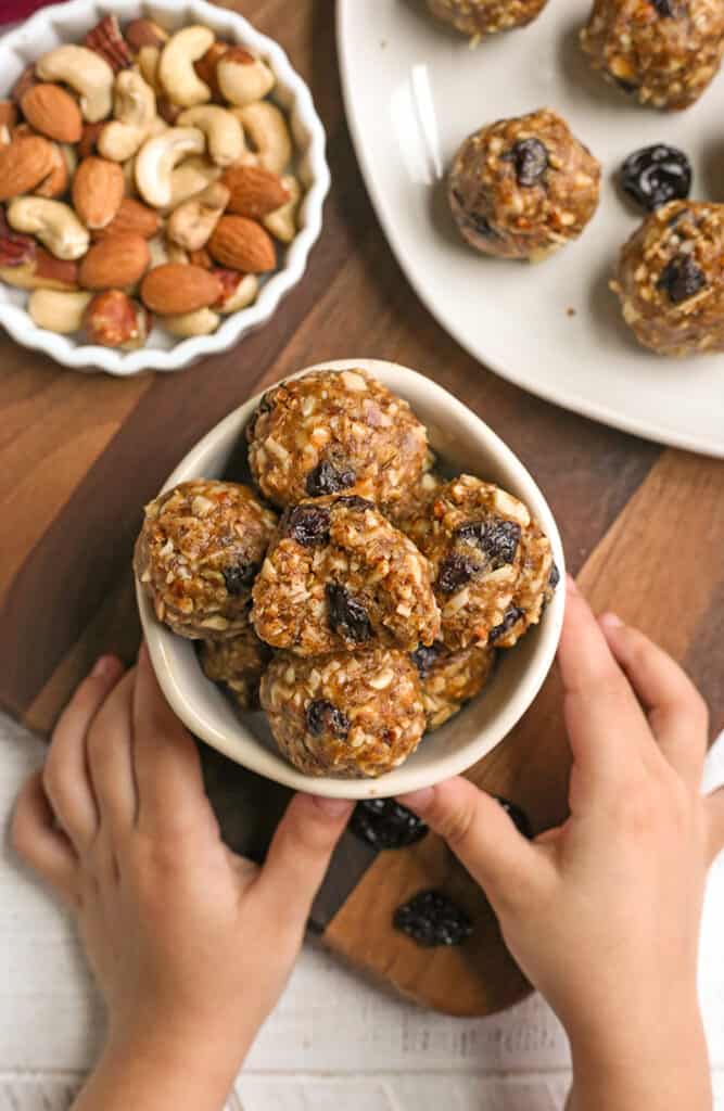 granola bites in a small bowl with two small hands holding it