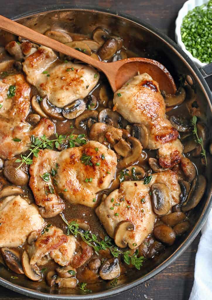 creamy mushroom chicken in a pan with a wooden spoon