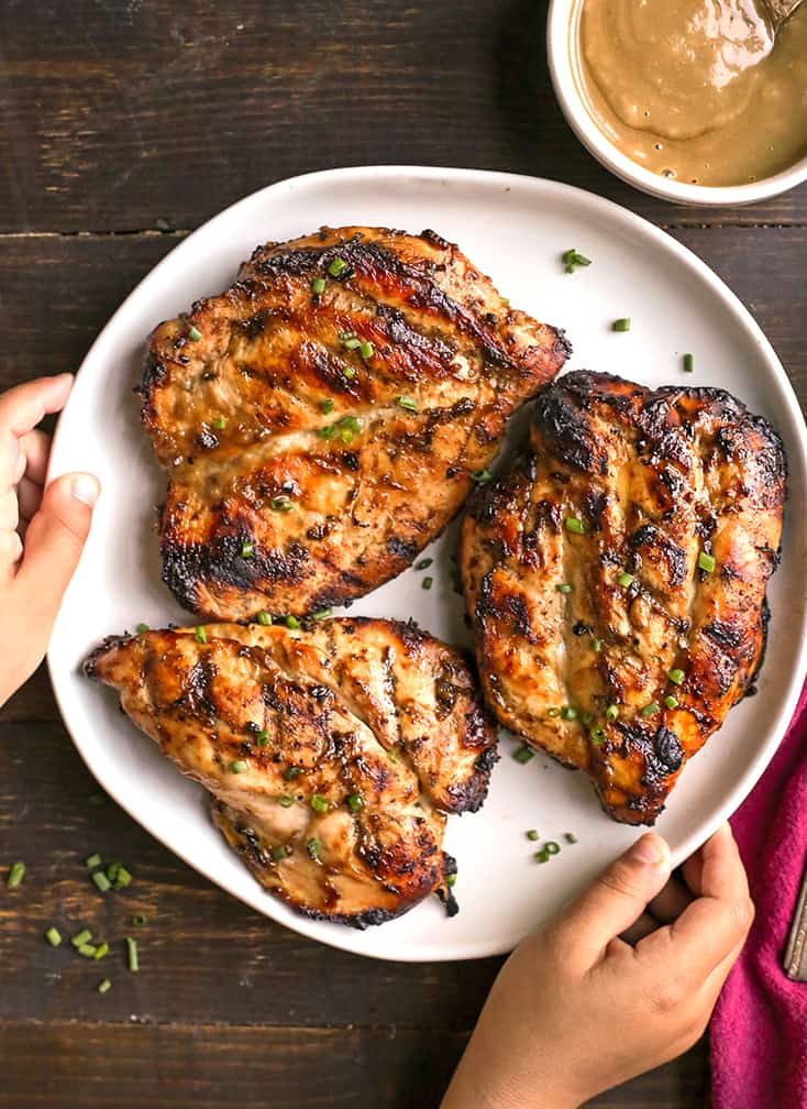 three pieces of grilled honey mustard chicken on a plate with little hands holding it 