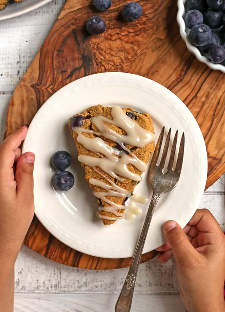 a paleo blueberry scone on a plate with little hands holding it