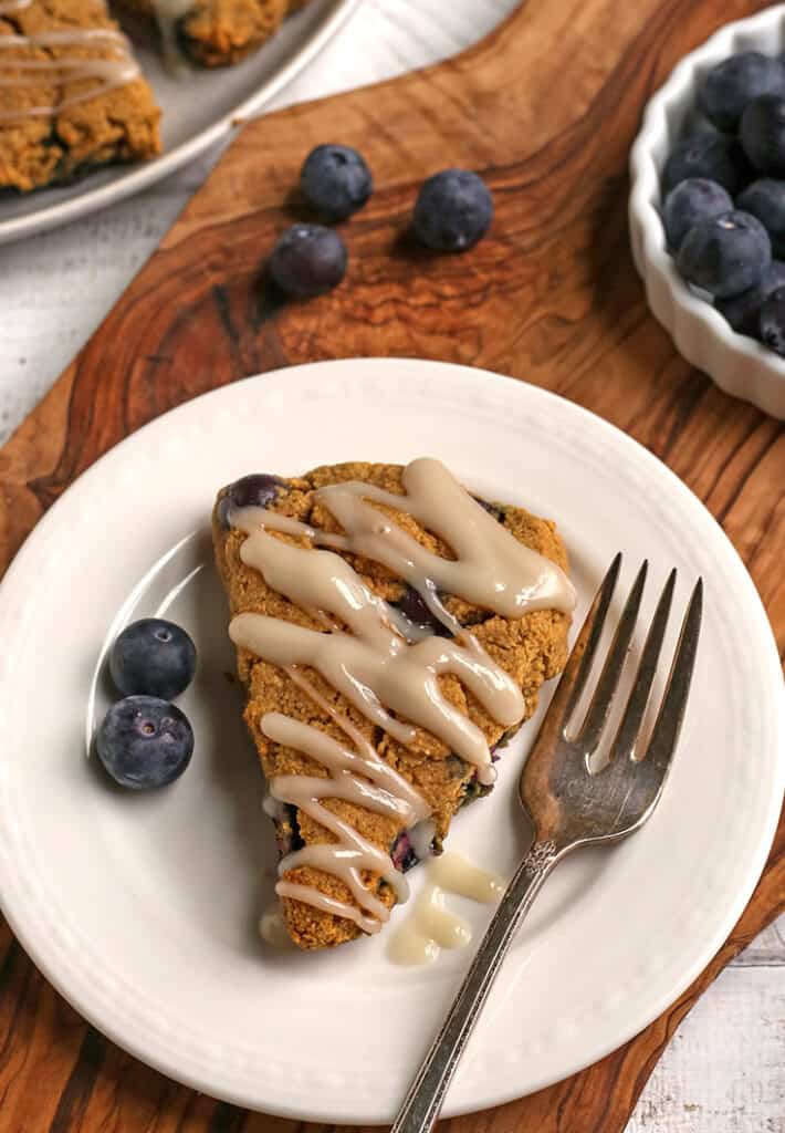 paleo blueberry scone on a plate with blueberries in the background