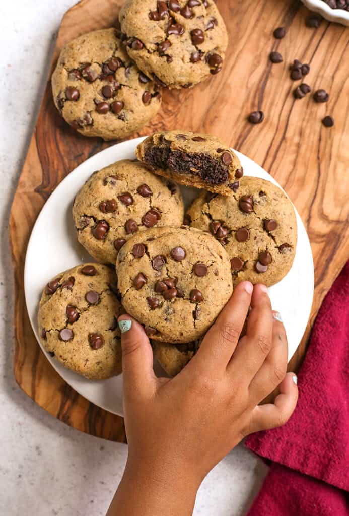 a little hand reaching for a vegan brownie stuffed chocolate chip cookie