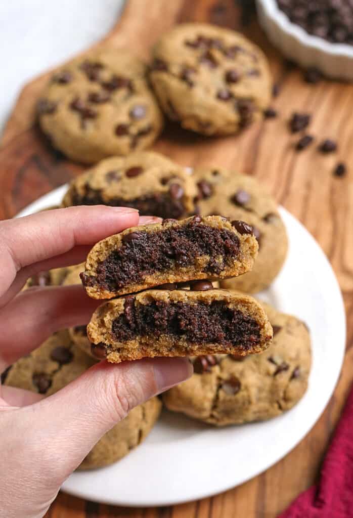 a hand holding a vegan chocolate chip cookie with a brownie center 