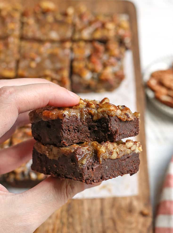 hand holding 2 paleo pecan praline brownies, one with a bite taken out of it