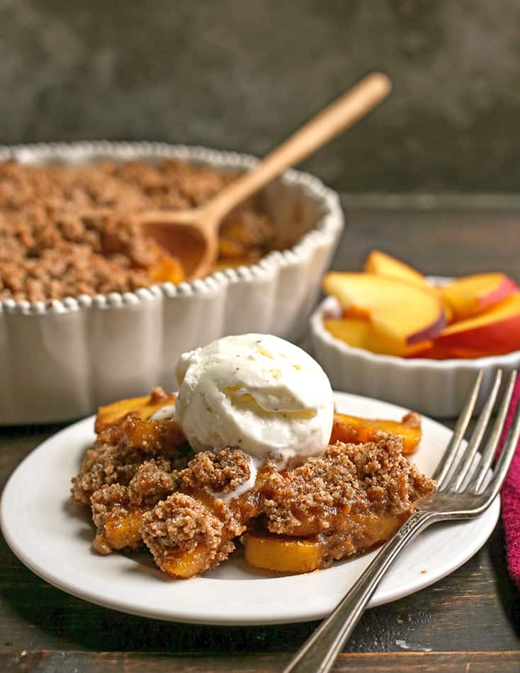 side shot of paleo vegan peach crisp on a plate with ice cream