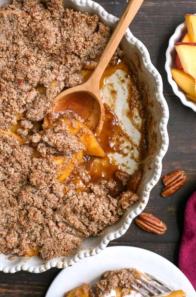 paleo vegan peach crisp in a pan with a scoop taken out