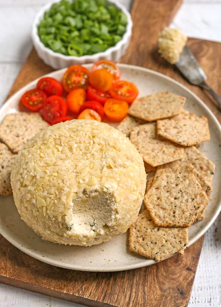 vegan paleo cheeseball on a plate with crackers, with a bite out of the cheeseball