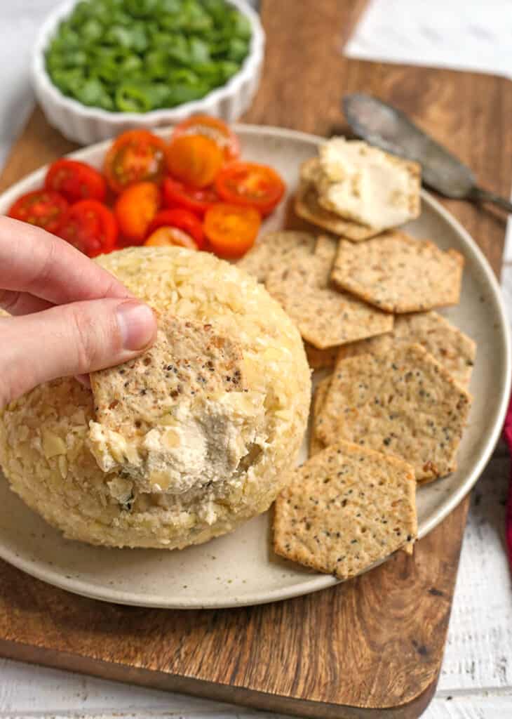 a hand dipping a cracker into a paleo vegan cheeseball