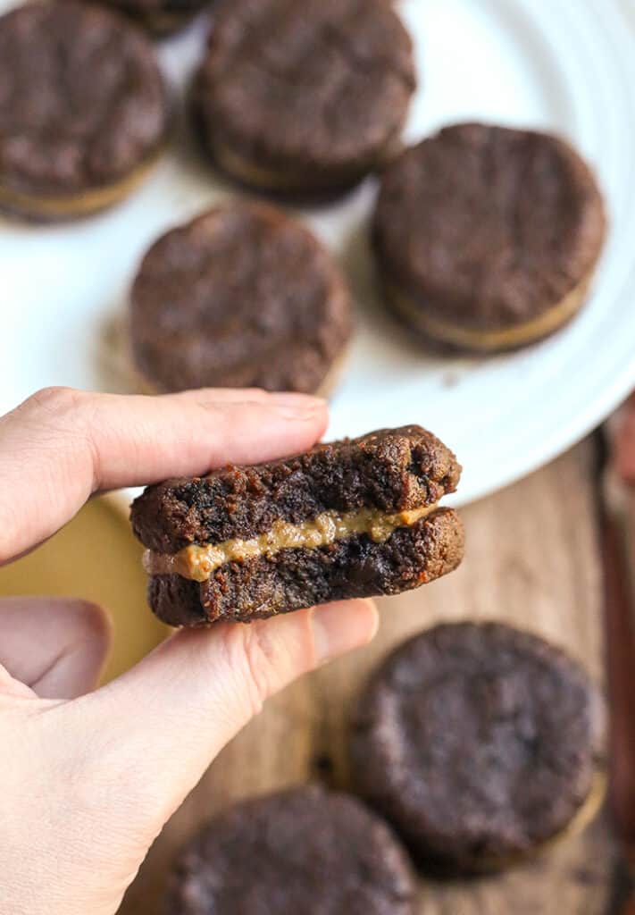 a hand holding a paleo chocolate sandwich cookie with a bite taken out of it 