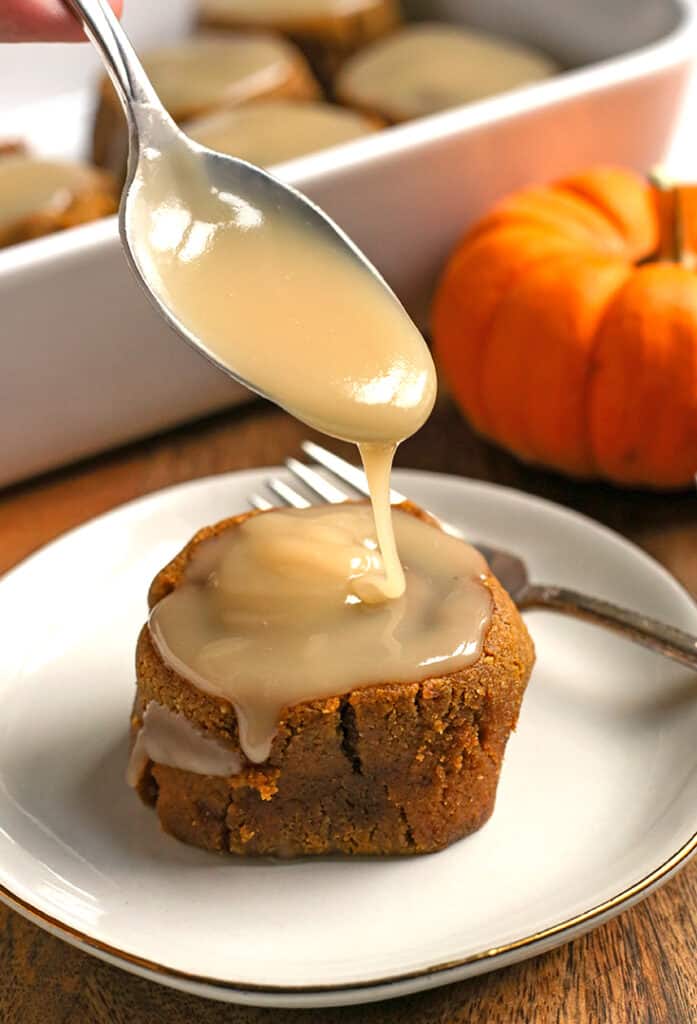 a spoon glazing a paleo pumpkin cinnamon roll