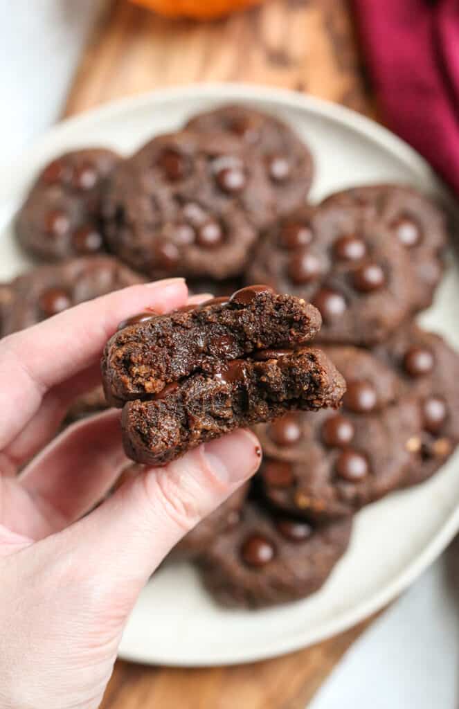 a hand holding two paleo pumpkin fudge cookies with a bite taken out of them 