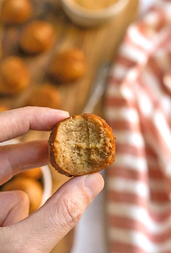 a hand holding a paleo vegan cinnamon roll bite with a bite taken out of it 