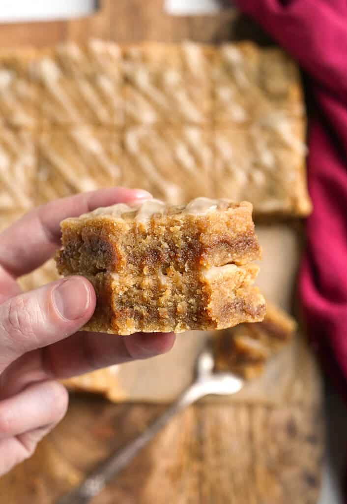 a hand holding two paleo cinnamon roll blondies with bites taken out 